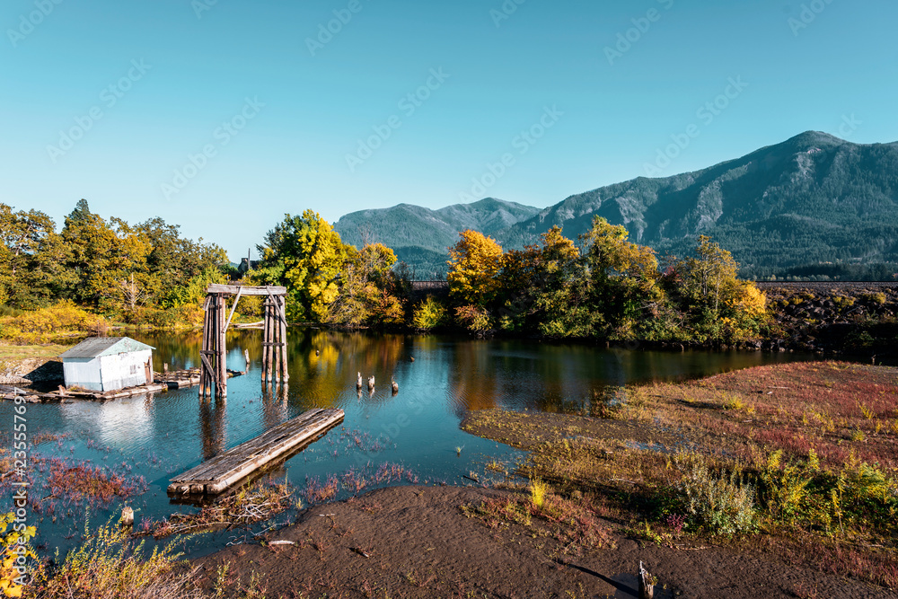 Autumn landscape with an old wooden pier and the barn and the mountains and the yellowed trees in the Bay of the Columbia River