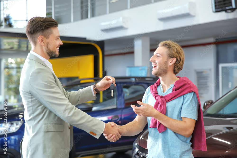 Obraz premium Salesman shaking hands with customer while giving car key in auto dealership