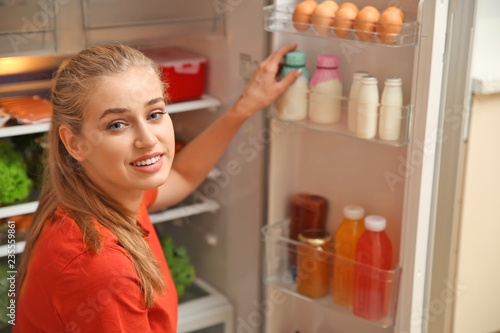 Young woman taking yogurt from refrigerator at home