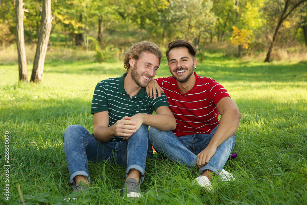 Portrait of happy gay couple sitting on grass in park Portrait of happy gay couple sitting on grass in park
