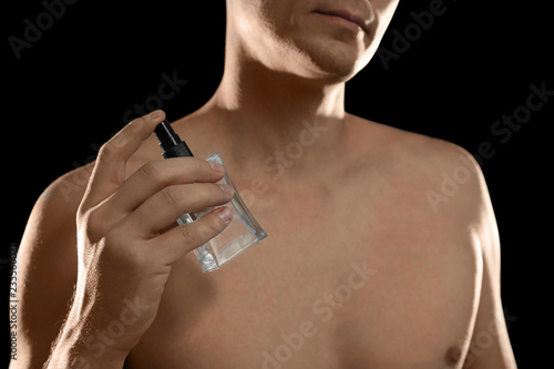 Young man using perfume on black background, closeup