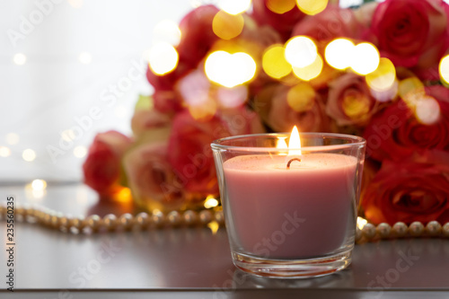 Burning candles with rose fresh flowers bouquet on gray table  close up home interior details with bokeh lights
