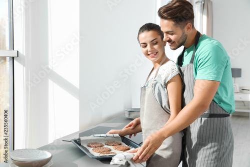 Young couple with oven sheet of homemade cookies in kitchen, space for text