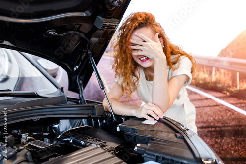 Redhead girl standing in front of a broken car on the road
