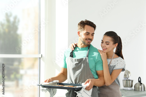 Young couple with oven sheet of homemade cookies in kitchen, space for text