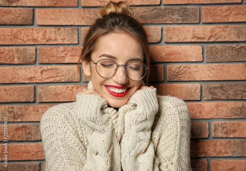 Beautiful young woman in warm sweater near brick wall