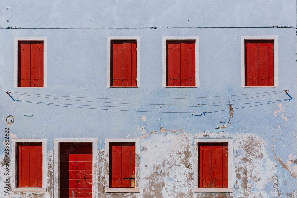 Red wooden windows and door on old light blue wall, on the island of Burano, in Venice, Italy Red wooden windows and door on old light blue wall, on the island of Burano, in Venice, Italy