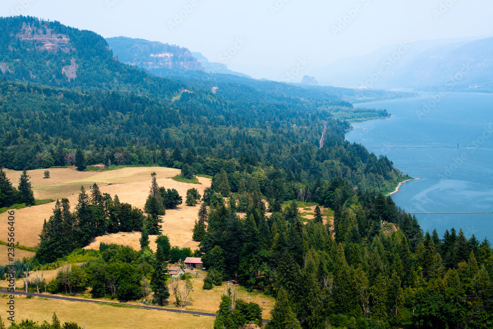 The mountainous coast of the winding Columbia River with trees and meadow with house in Columbia River Gorge