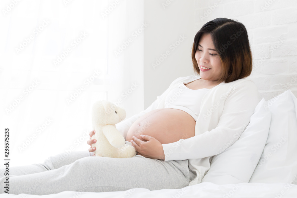 Pregnant woman with teddy bear on white bed Pregnant woman with teddy bear on white bed
