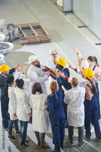 Group of angry factory workers attacking business executives during strike meeting in industrial workshop photo