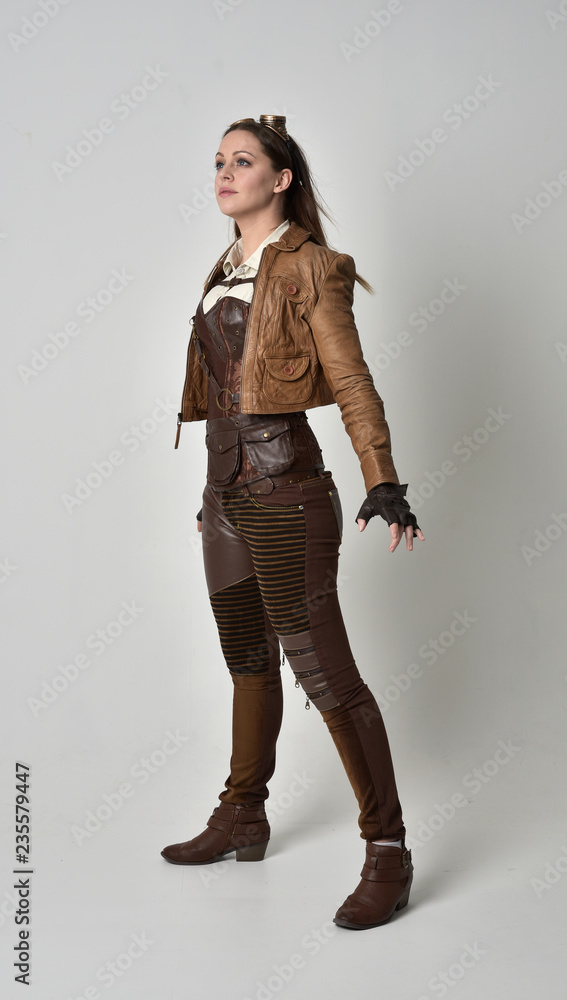 full length portrait of brunette girl wearing brown leather steampunk outfit. standing pose, on grey studio background. full length portrait of brunette girl wearing brown leather steampunk outfit. standing pose, on grey studio background.