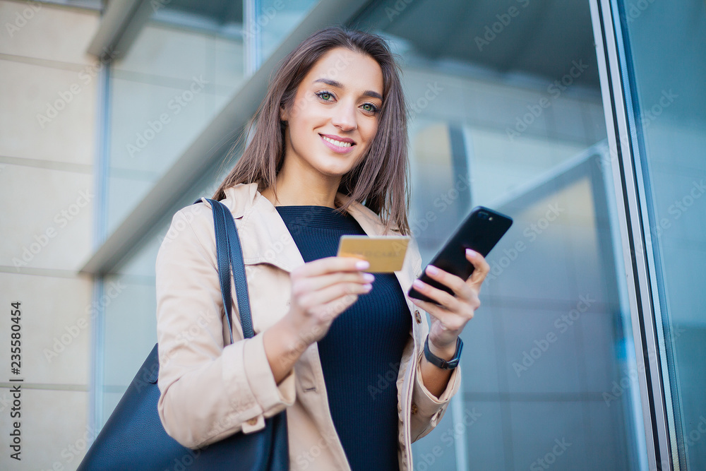 Low Angle Of Pleased Girl Standing at the Airport Hall. He is Using Gold Credit card and Cellphone For Paying Low Angle Of Pleased Girl Standing at the Airport Hall. He is Using Gold Credit card and Cellphone For Paying