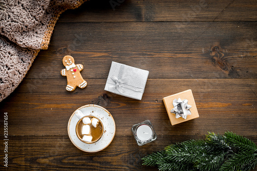 Romantic winter composition with hot drink. New Year or Christmas Eve. Cocoa with marshmallow, gift box, gingerbread man, wool blanket, fir branches on dark wooden background top view copy space
