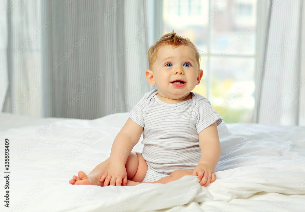 Charming blue-eyed baby 10 months in bed in a striped jumpsuit Charming blue-eyed baby 10 months in bed in a striped jumpsuit