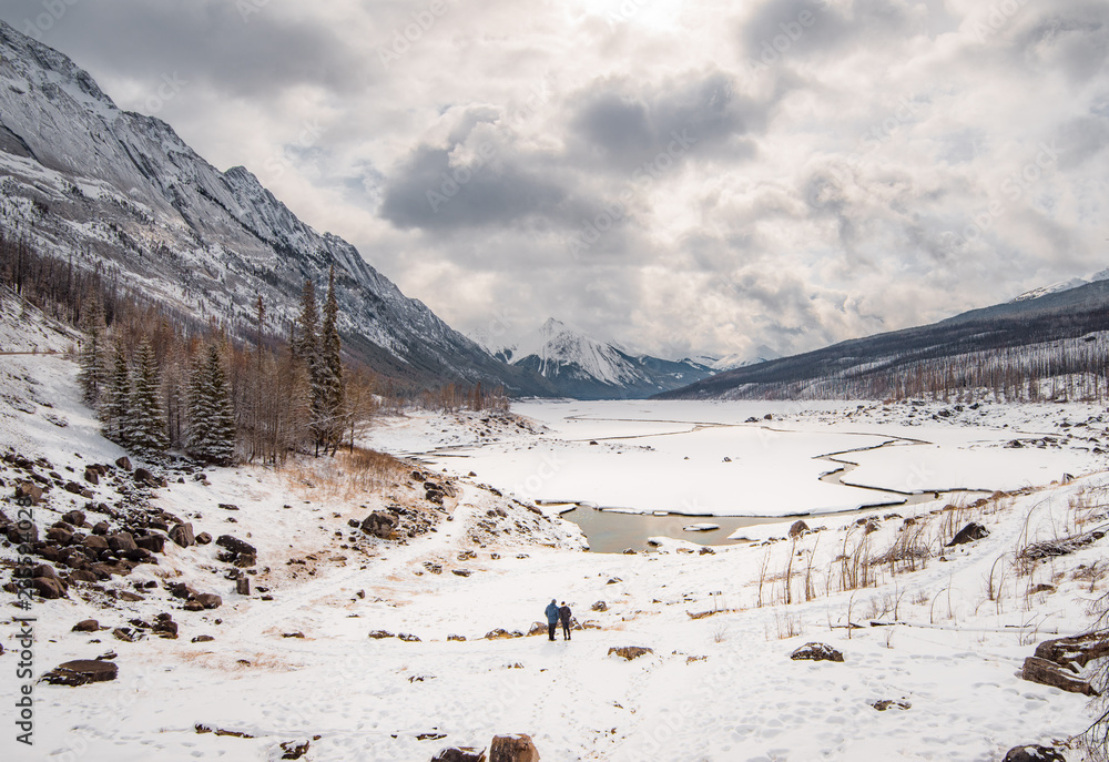 A couple stands on the edge of a snow covered lake with a thawing center on a partly cloudy day