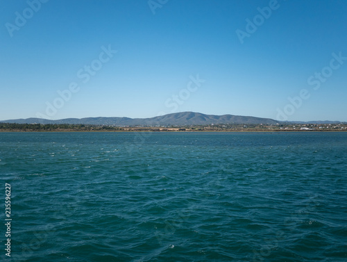 Coast of Algarve, Portugal from the ocean, with hills in distance.