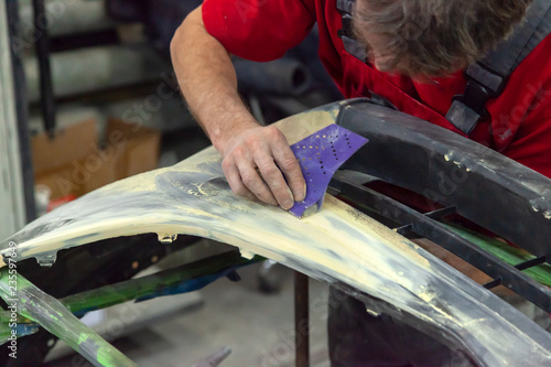 фотографія A man prepares a car body element for painting after an accident with the help of abrasive paper in a car repair shop