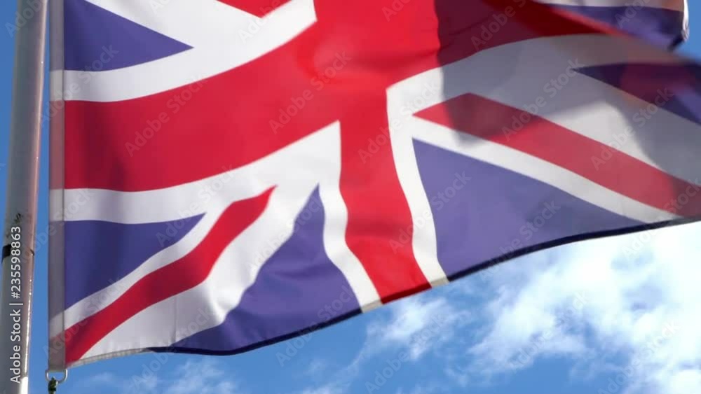 Slow motion of english flag waving in the wind on flagpole at an city. Slow-motion of England banner flutters at day in front of blue sky. Close up of a real fabric texture ensign fluttering-Dan Slow motion of english flag waving in the wind on flagpole at an city. Slow-motion of England banner flutters at day in front of blue sky. Close up of a real fabric texture ensign fluttering-Dan