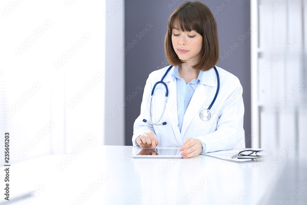Doctor woman at work. Female physician using tablet computer while sitting at the desk in clinic or hospital. Medicine and healthcare concept for advertising Doctor woman at work. Female physician using tablet computer while sitting at the desk in clinic or hospital. Medicine and healthcare concept for advertising