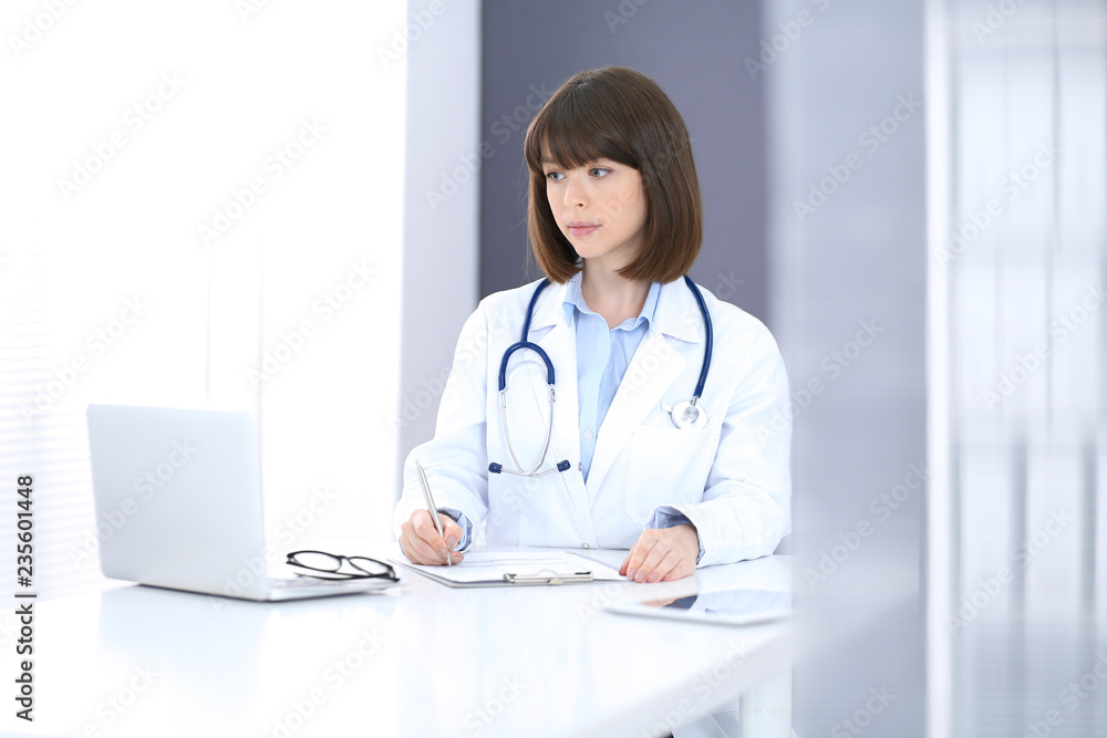 Doctor woman at work. Female physician filling up medical form while sitting at the desk in clinic or hospital. Medicine and healthcare concept for advertising Doctor woman at work. Female physician filling up medical form while sitting at the desk in clinic or hospital. Medicine and healthcare concept for advertising