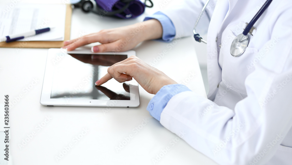 Woman doctor using tablet computer while sitting in hospital office closeup. Healthcare, insurance and medicine concept Woman doctor using tablet computer while sitting in hospital office closeup. Healthcare, insurance and medicine concept