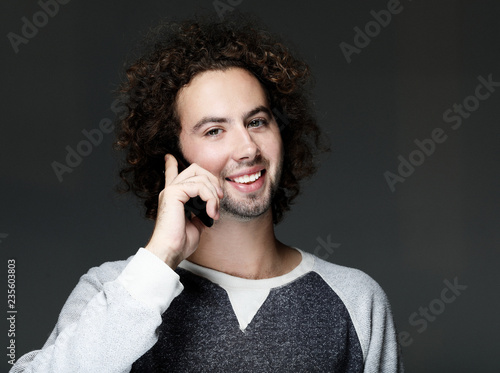 Smiling young man talking by smartphone and looking at the camera