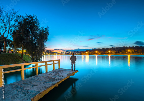 Da Lat, Vietnam - October 29th, 2018: Man standing on a small bridge reflecting on the lake at sunrise as a relaxing way to welcome the beautiful new day © huythoai