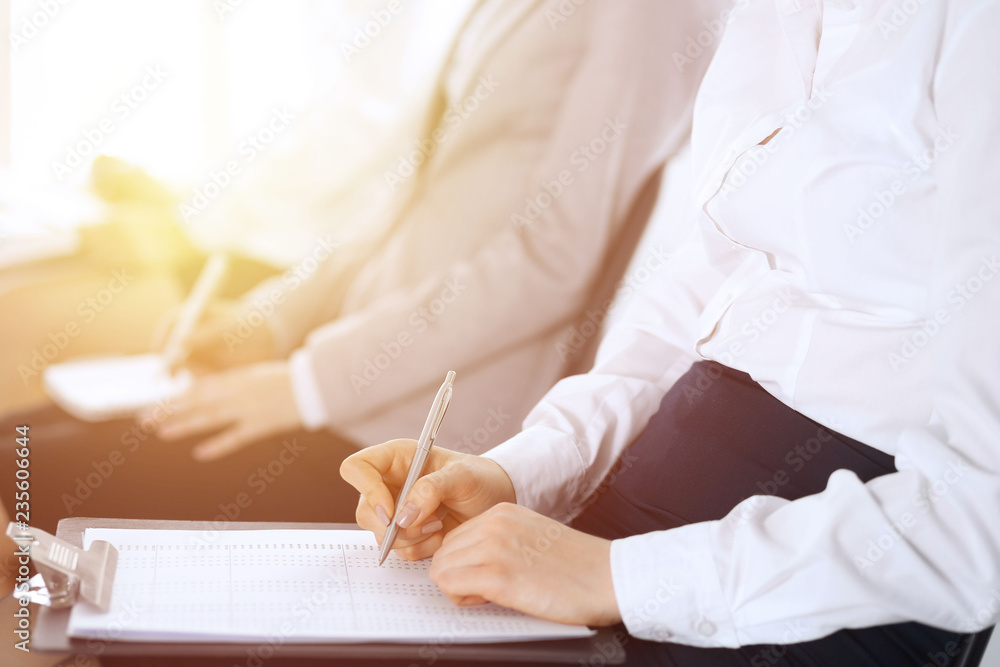 Business people taking part at conference or training at office, close-up. Women sitting on chairs and making notes like at queue or meeting Business people taking part at conference or training at office, close-up. Women sitting on chairs and making notes like at queue or meeting