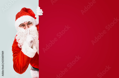 Santa Claus with finger on lips asking for silence with colorful advertisement board and copy space © Sergey Peterman