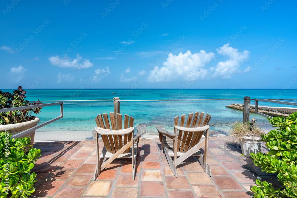 Wooden chairs facing the clear tropical ocean, summertime concept