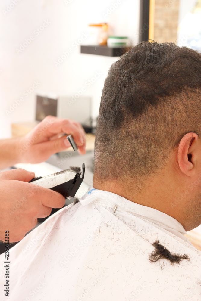 Fototapeta premium Back view of man getting short hair trimming at barber shop with clipper machine
