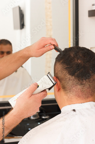 Back view of man getting short hair trimming at barber shop with clipper machine