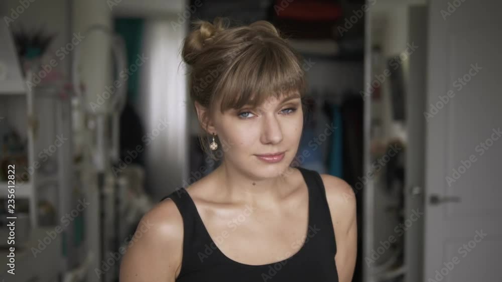 Young beautiful mischievous blonde woman in black t-shirt with high buns hairstyle having fun in bedroom at home. Smiling, looking into camera, posing. Young beautiful mischievous blonde woman in black t-shirt with high buns hairstyle having fun in bedroom at home. Smiling, looking into camera, posing.