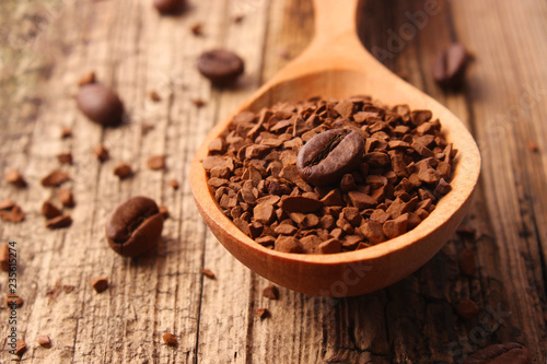 instant coffee in a wooden spoon and coffee beans on a wooden background.