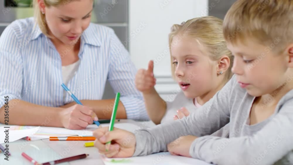Rack focused shot of little daughter and son drawing at table together with beautiful blonde mother Rack focused shot of little daughter and son drawing at table together with beautiful blonde mother
