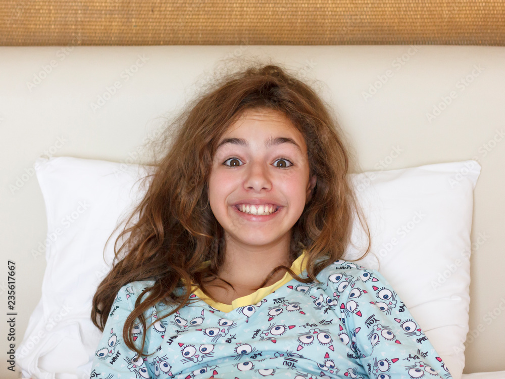 Just awake pretty teenager girl with funny emotion face and wild hair on the bed Just awake pretty teenager girl with funny emotion face and wild hair on the bed