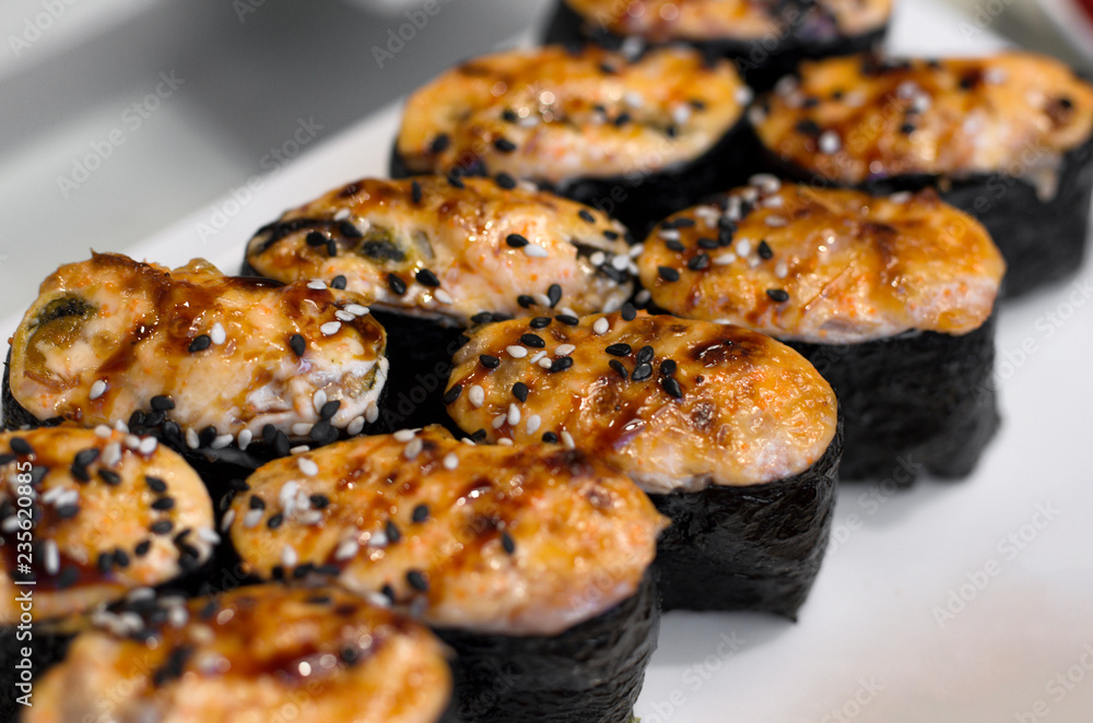 Baked Japanese sushi rolls sprinkled with sesame seeds close-up with blurred background