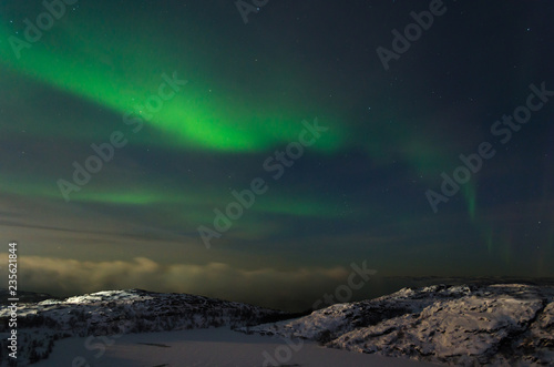 Beautiful northern lights, aurora in the night sky over the snow-covered hills. © Moroshka