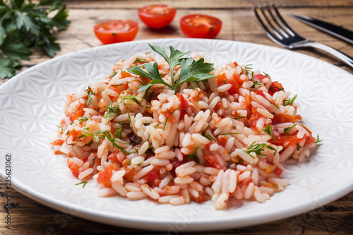 Rice with tomato sauce and greens on wooden background.