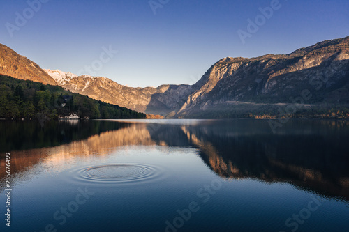 Sunrise view of alpine lake Bohinj with blue sky, sunlight and mist over water. Circles in water. Famous lake of Bohinj in Triglav National Park, Julian alps, Slovenia.