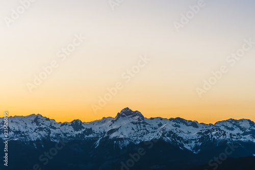 Sunset over the Julian alps and the highest mountain of Slovenia Triglav. Orange sky and alpine landscape on horizont. Snow covered summit of Mount Triglav with sunstar. Wallpaper or background.