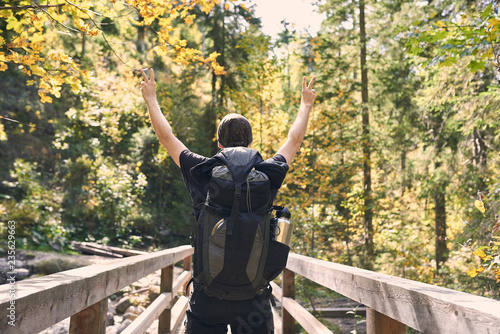 Mann von hinten in Siegerpose auf einer Brücke im Wald, genießt die Freiheit