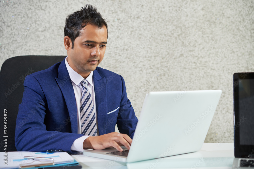 Serious young office worker concentrated on his work at office, he sitting at the table and typing on laptop Serious young office worker concentrated on his work at office, he sitting at the table and typing on laptop
