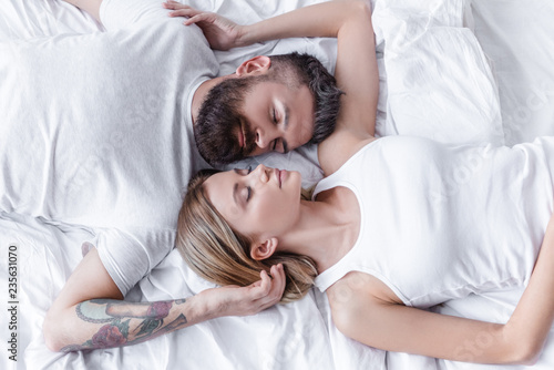 pretty couple in love lying head to head and sleeping in white bed
