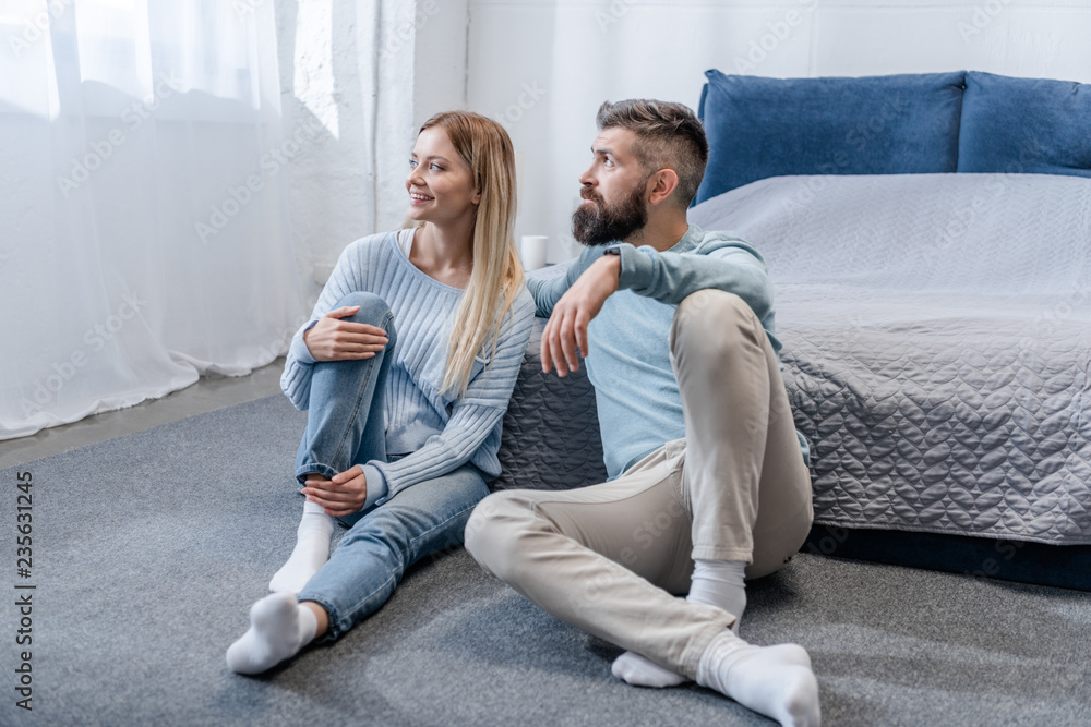 happy young couple sitting on floor and looking at window in blue bedroom happy young couple sitting on floor and looking at window in blue bedroom