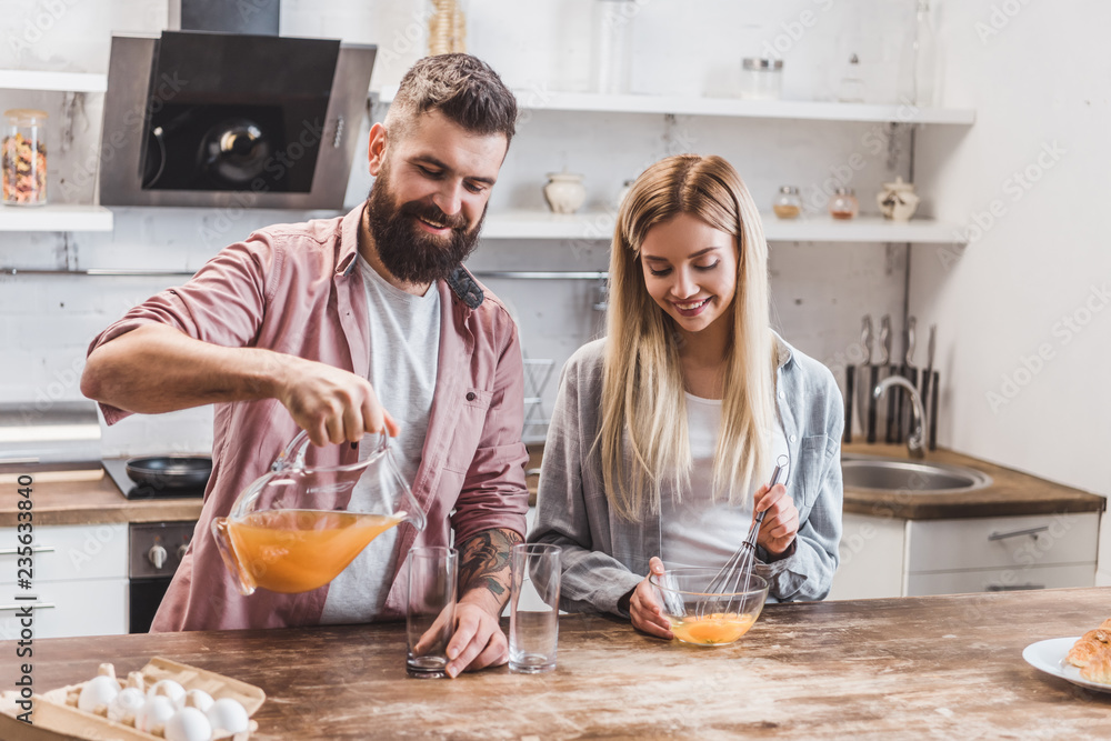 young couple preparing breakfast together at kitchen and drinking juice young couple preparing breakfast together at kitchen and drinking juice