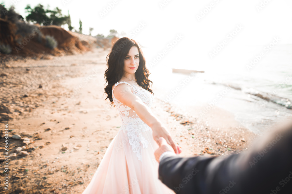 Wedding couple, groom, bride with bouquet posing near sea and blue sky Wedding couple, groom, bride with bouquet posing near sea and blue sky