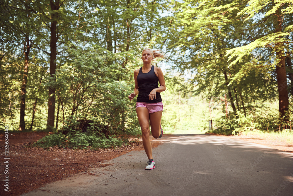 Young woman jogging alone along a path in the forest Young woman jogging alone along a path in the forest