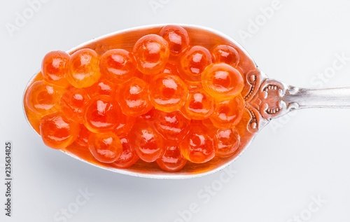 Red caviar on silver spoon isolated on white background close-up. Top view.