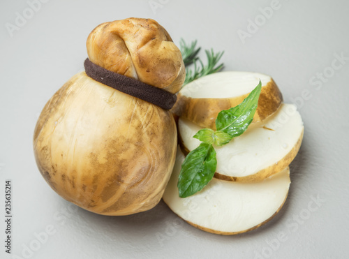 Traditional Italian smoked Scamorza cheese with herbs on gray background.